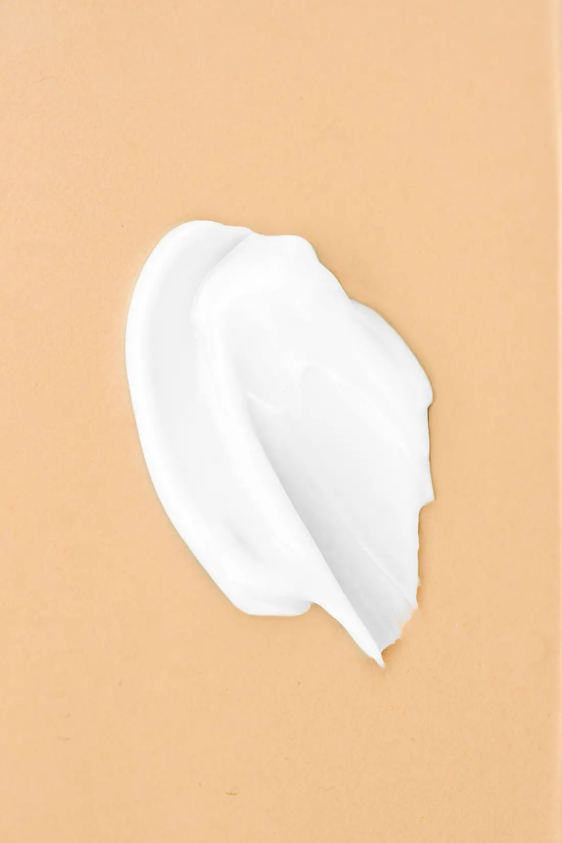 A single swipe of white cream on a peach background.