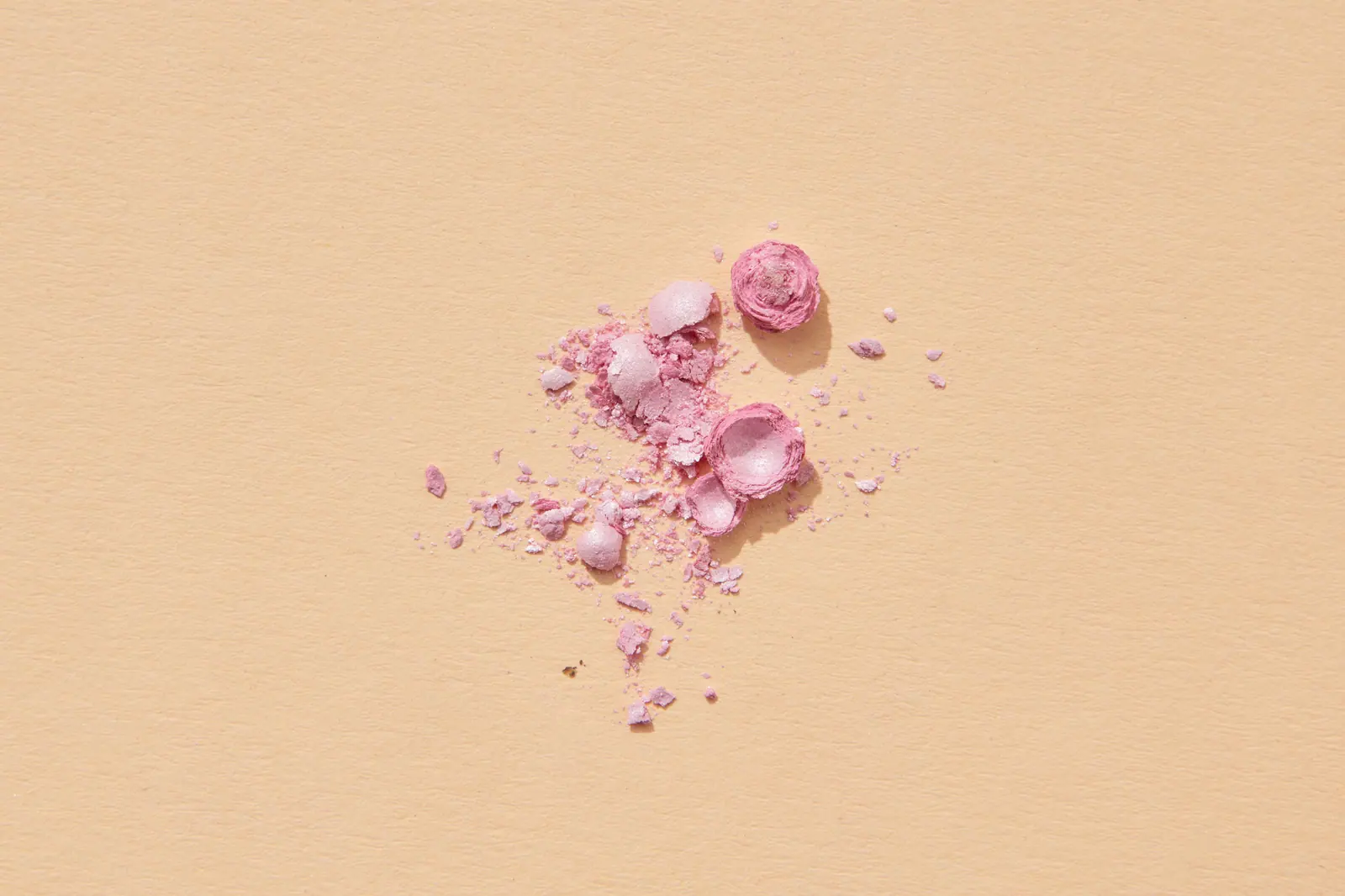Fragments of pink blush powder on a warm beige surface.