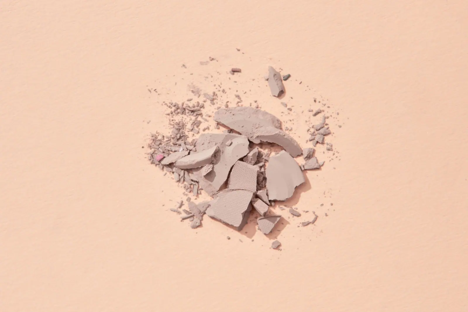 Crushed pale pressed powder scattered across a soft peach surface.